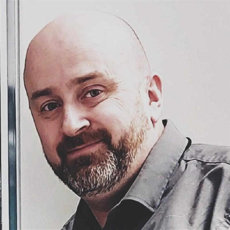 Headshot image of Brian Shaw, wearing a grey collared shirt, looking into the camera.