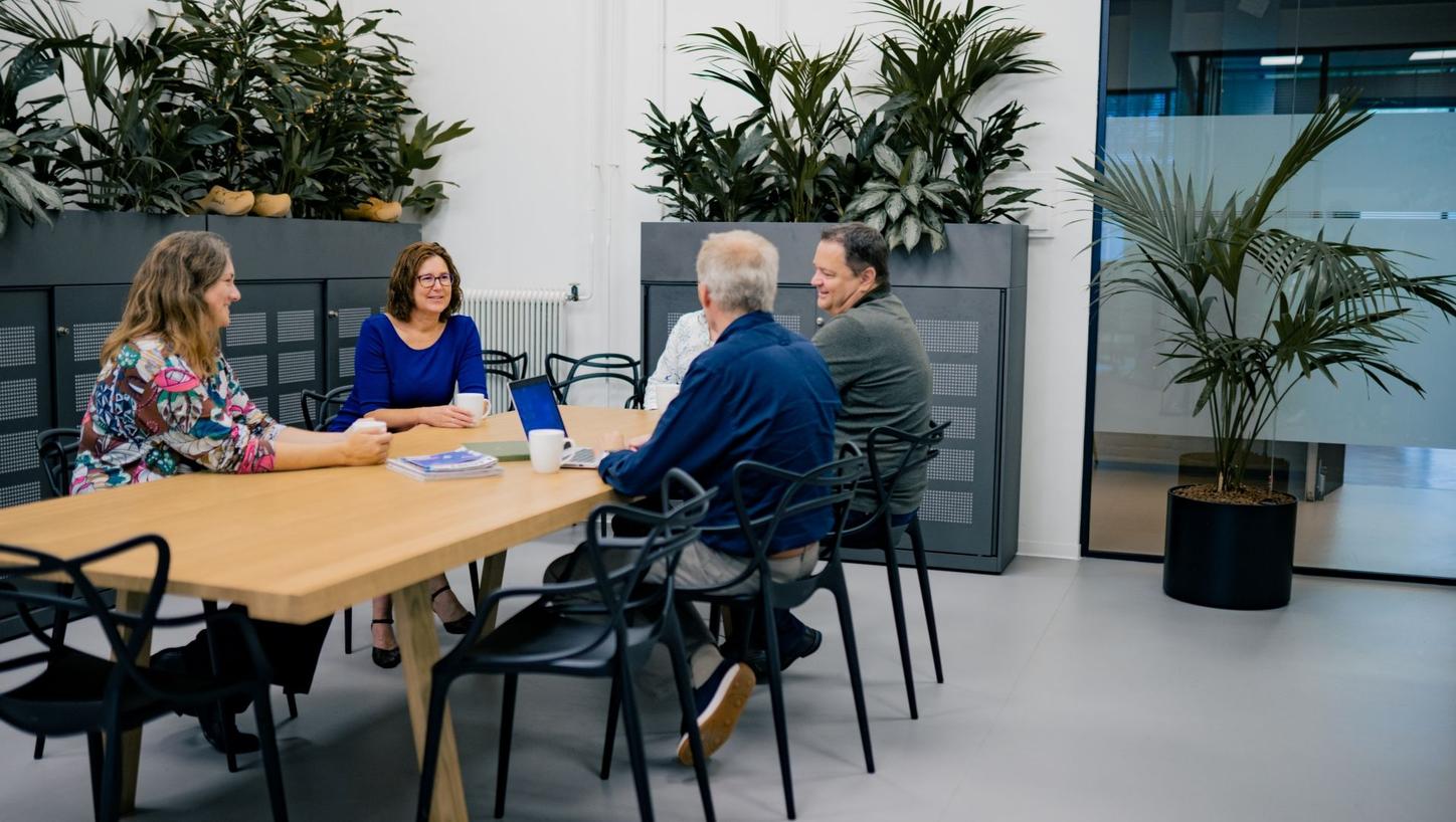 Femke sitting at a table in the office kitchen together with four of her colleagues, chatting, taking a break