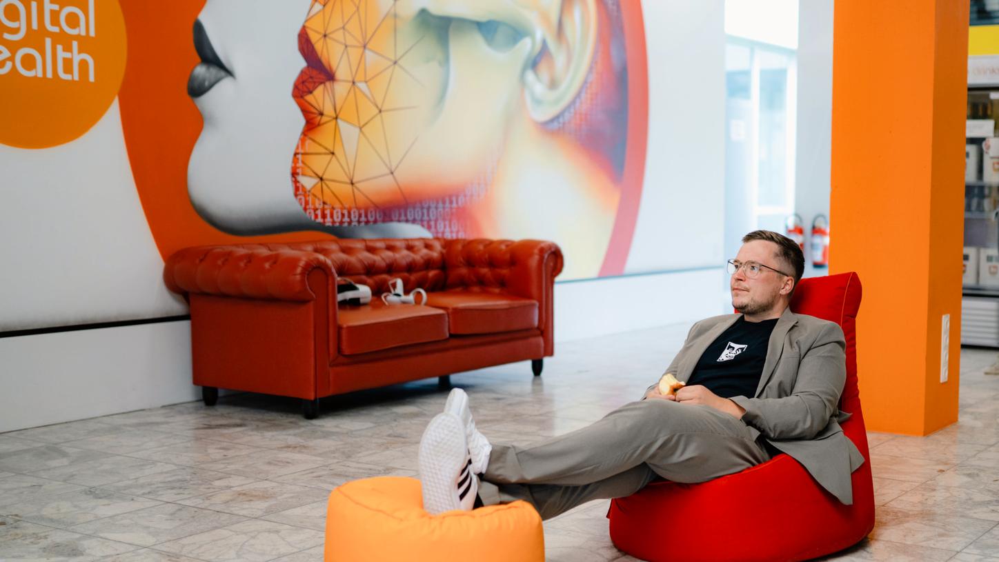 Anton is sitting relaxed on a beanbag chair. He has placed his outstretched feet with sneakers on a seat cushion.
