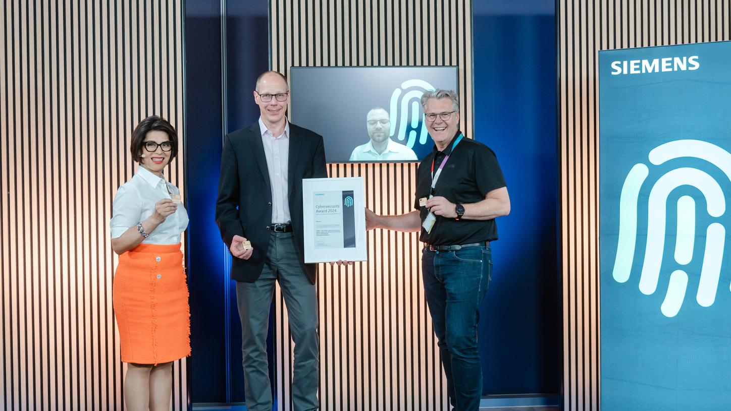 Three people stand on a stage at a Siemens event, holding a framed "Cybersecurity Award 2024" certificate.