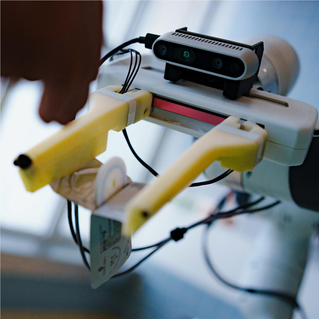 Close-up of the RGBD camera and the gripper of the AURORA assistant robot prototype. The robot opens the sterile packaging of a surgical suture set.