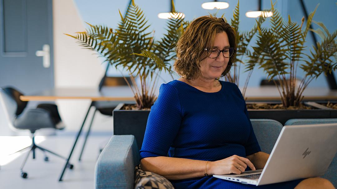 Femke sitting in the Lobby on a couch with her laptop typing and smiling